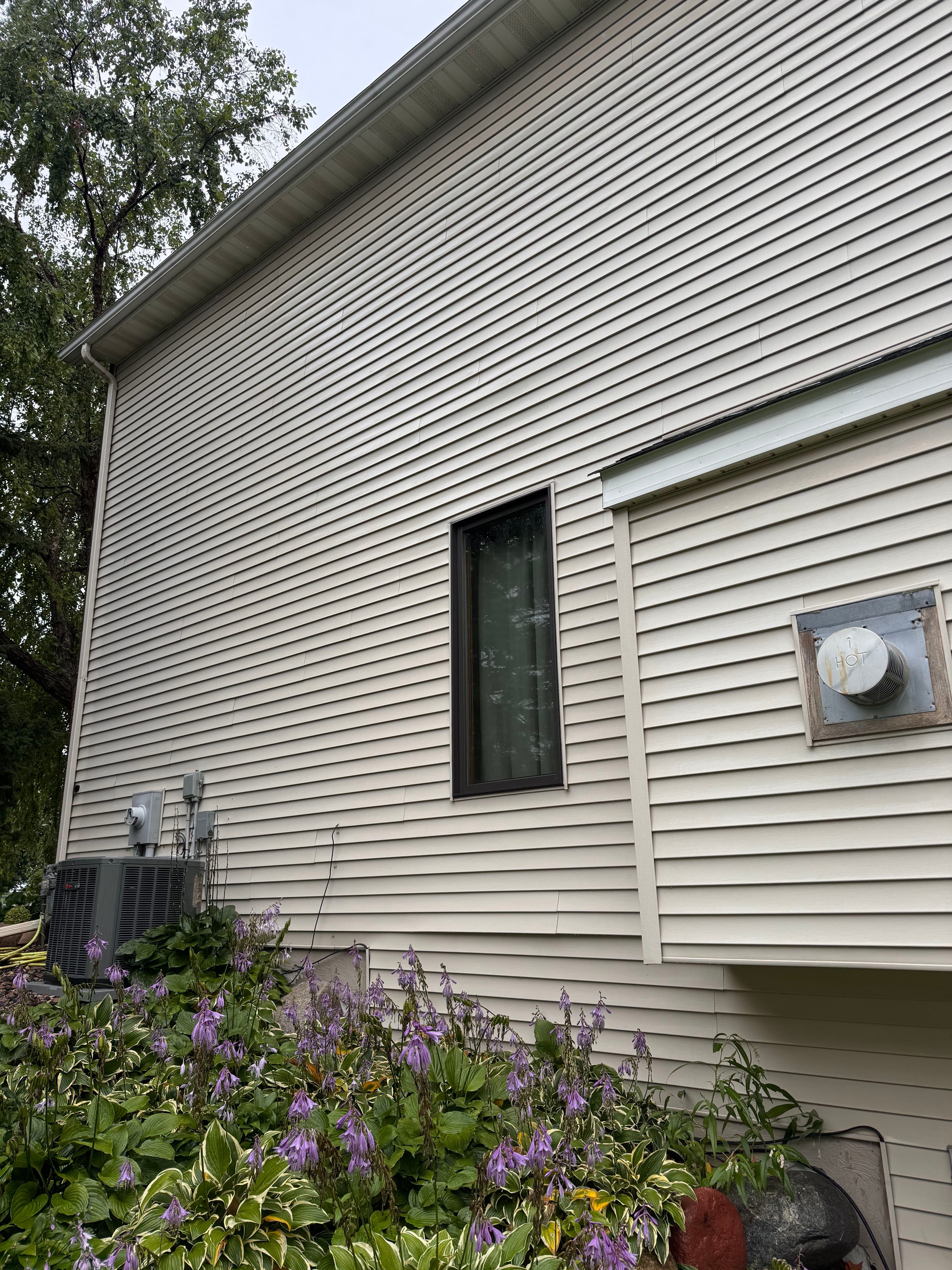 Side view of a house with beige siding, window, and flower garden in foreground.