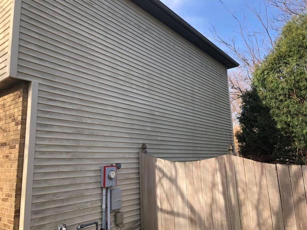 Side view of a house with beige siding and a wooden fence in the foreground.